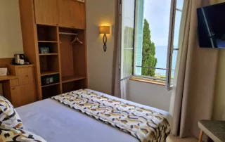 Chambre double avec vue mer, grand placard en bois, TV murale et fenêtre ouverte sur la Méditerranée.