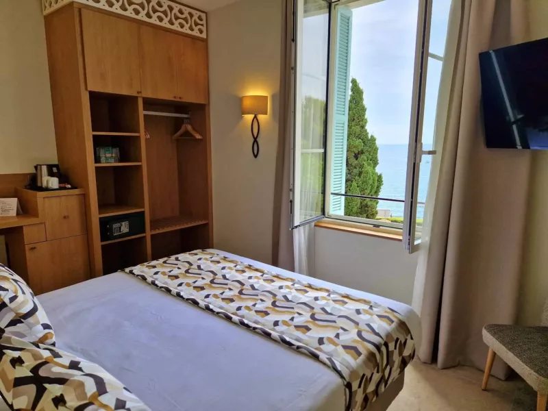Chambre double avec vue mer, grand placard en bois, TV murale et fenêtre ouverte sur la Méditerranée.